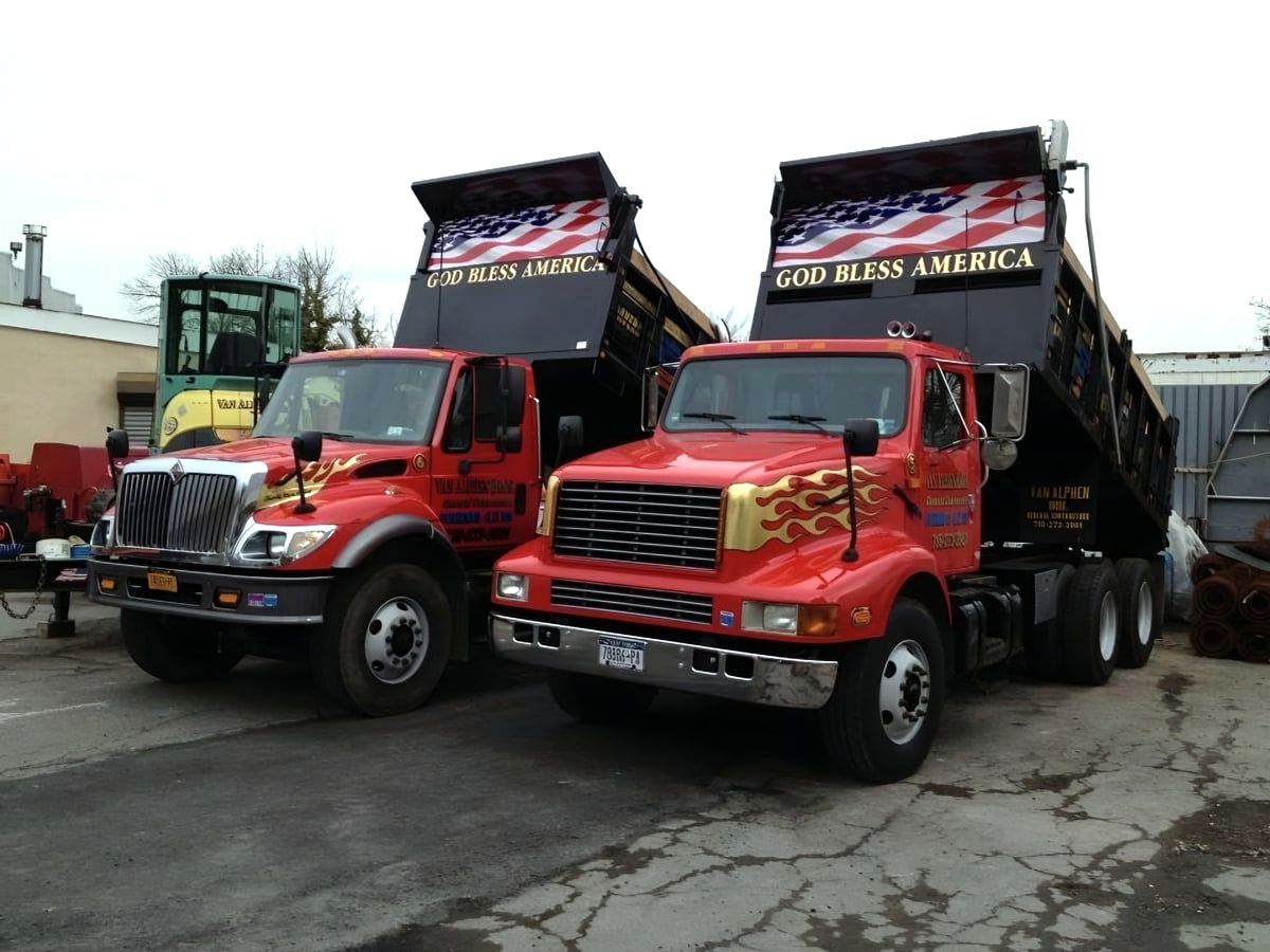 Two red dump trucks with raised beds reading God Bless America